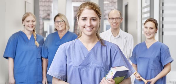 Eine junge Pflegerin in der Geburtshilfe im Vordergrund, im Hintergrund drei andere Pflegerinnen und ein Arzt