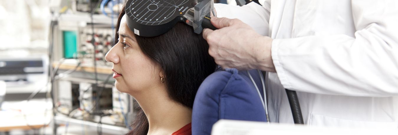 Probandin wird eine Stimulationsspule Transkranille Magnetstimulation an den Kopf gehalten
