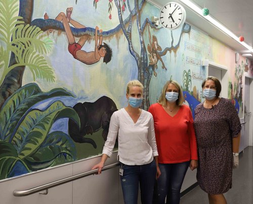 Die Pflegekräfte Daniela Fülle, Ramona Nagy-Obreja und Oberärztin Dr. Melanie Kapapa vor einer bemalten Wand. 