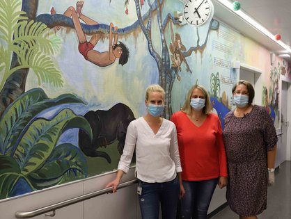 Die Pflegekräfte Daniela Fülle, Ramona Nagy-Obreja und Oberärztin Dr. Melanie Kapapa vor einer bemalten Wand. 