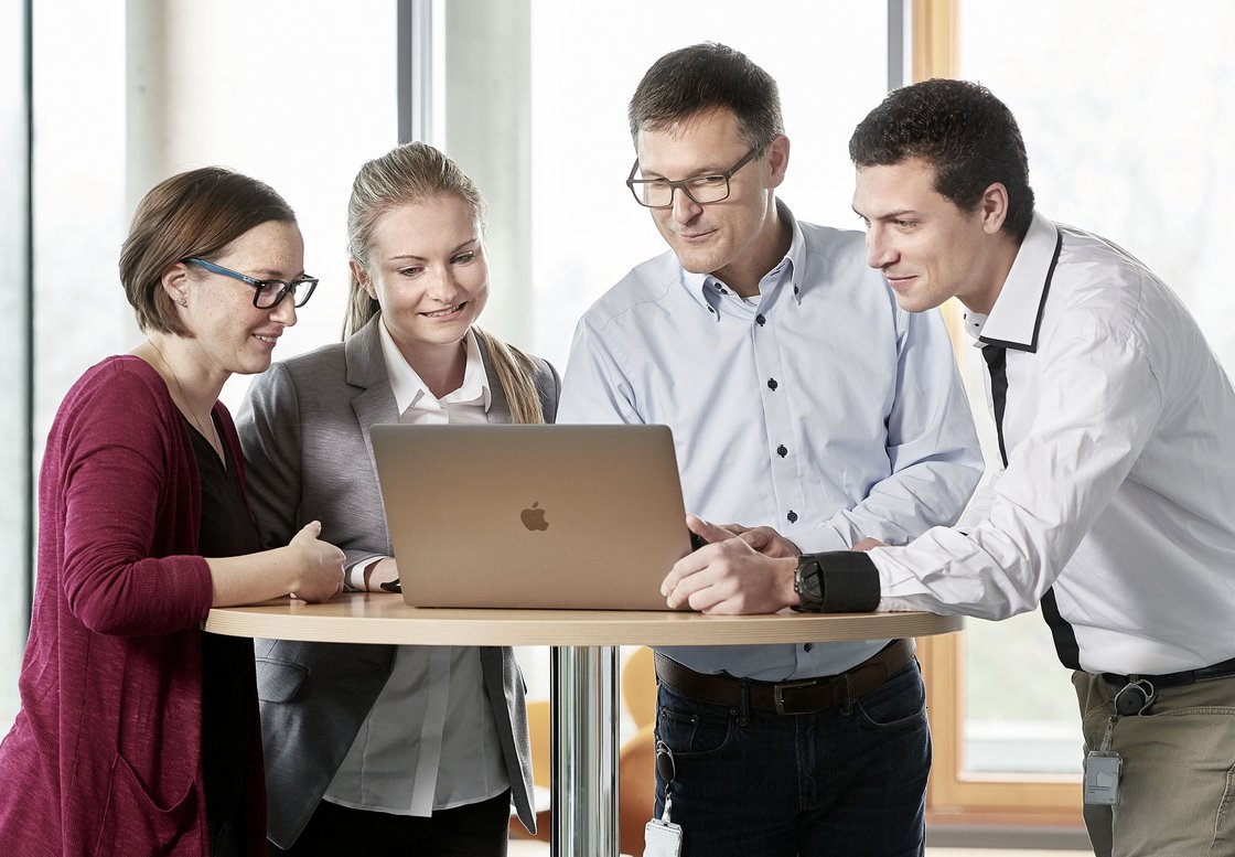 Zwei Mitarbeiterinnen und zwei Mitarbeiter aus der Verwaltung stehen vor einem Laptop