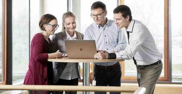 Zwei Mitarbeiterinnen und zwei Mitarbeiter aus der Verwaltung stehen vor einem Laptop