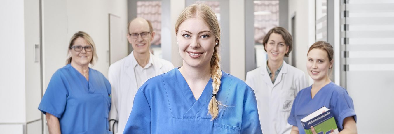 Eine Mitarbeiterin aus der Pflege steht im Vordergrund, im Hintergrund stehen zwei Ärzte und zwei Pflegekräfte