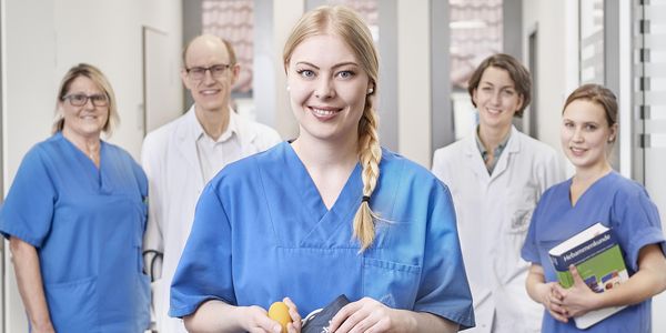 Eine weibliche Pflegekraft im Vordergrund, im Hintergrund zwei andere Pflegekräfte und zwei Ärzte