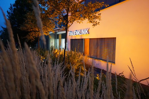 Außenansicht der Universitätsfrauenklinik. Das Gebäude ist Orange beleuchtet