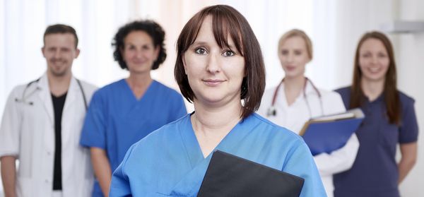 Eine weibliche Pflegekraft im Vordergrund, im Hintergrund zwei Ärzte und zwei andere Pflegekräfte