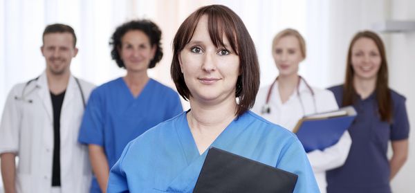 A female carer in the foreground, two doctors and two other carers in the background