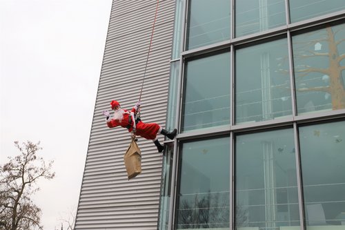 Der Nikolaus winkt den jungen Patient*innen zu, während er sich von der Klinikfassade der Kinder- und Jugendpsychiatrie abseilt.