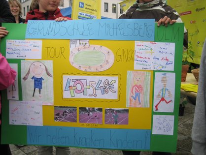 Scheck der Michelsberg-Grundschüler, den sie am 30.6.2011 im Beisein von Landrat Heinz Seiffert, Ivo Gönner, Oberbürgermeister der Stadt Ulm, und Prof. Dr. Daniel Steinbach, Oberarzt an der Ulmer Universitätsklinik für Kinder- und Jugendmedizin, an die Aktion „Hand in Hand“ des Förderkreises für tumor- und leukämiekranke Kinder Ulm e.V. übergeben haben (Foto: NN).
