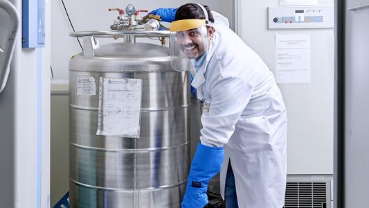 Ein Wissenschaftler mit Gesichtsschutz neben einem großen Tank aus Metall
