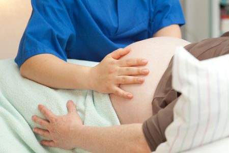 Pflegekraft untersucht den Bauch einer Schwangeren 