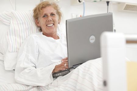 Patientin sitzt mit einem Laptop im Bett 