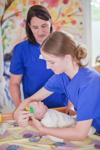Zwei Hebammen messen den Kopfumfang bei einer Baby-Puppe