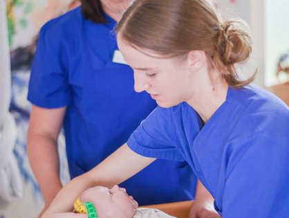 Zwei Hebammen messen den Kopfumfang bei einer Baby-Puppe