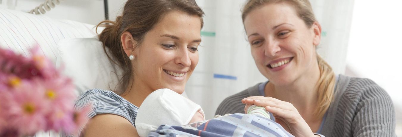 Mutter mit Baby im Arm und Besuch am Patientenbett