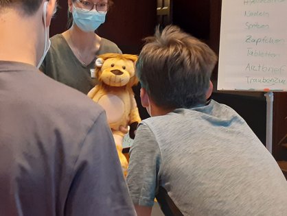 Eine Mitarbeiterin der Kinderklinik erklärt zwei Kindern spielerisch ihre Diagnose.