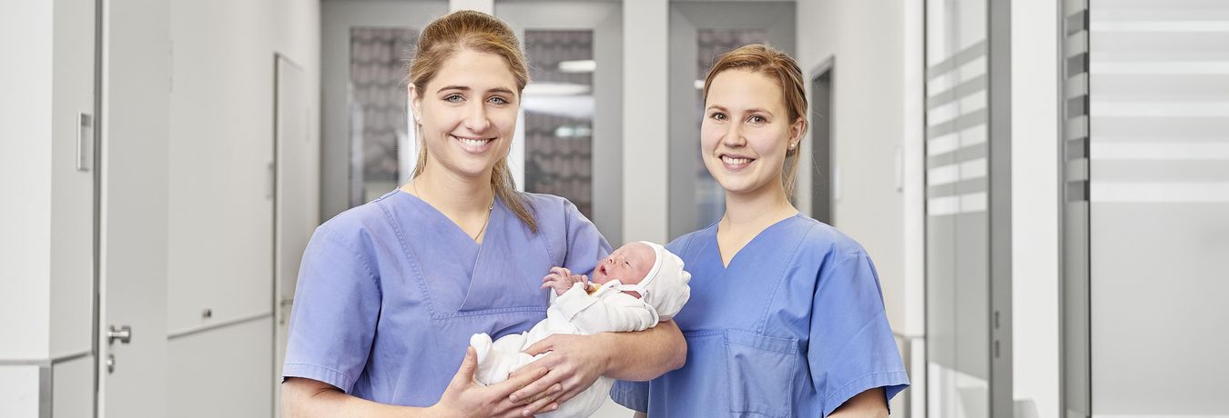 Zwei Pflegerinnen der Geburtshilfe mit einem Baby im Arm
