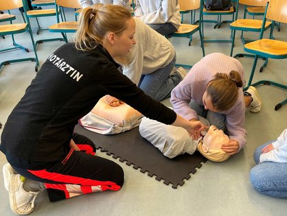 Eine Notärztin des UKU zeigt den Schüler*innen des Schubart-Gymnasiums an einem Dummie, wie man einen Menschen wiederbelebt. 