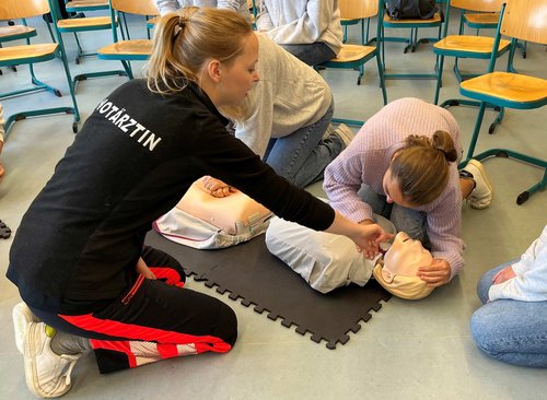 Eine Notärztin des UKU zeigt den Schüler*innen des Schubart-Gymnasiums an einem Dummie, wie man einen Menschen wiederbelebt. 