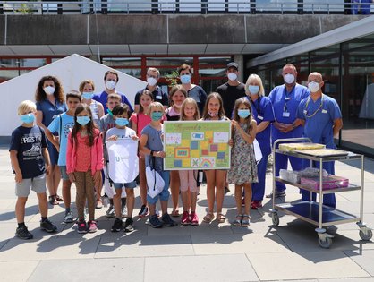 Gruppenbild bei der Kuchenübergabe von den elf Schüler*innen und dem Team der IOI vor dem Uniklinikum Ulm