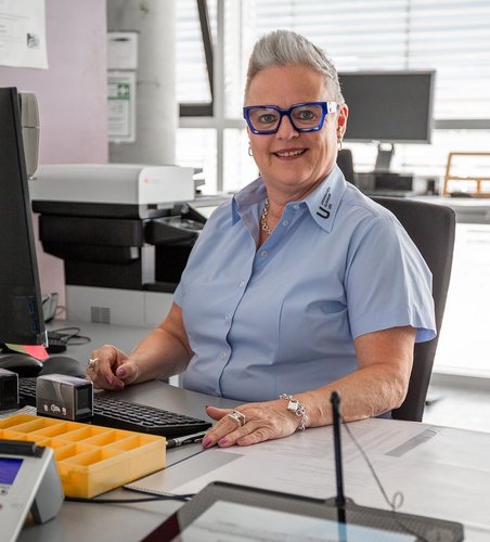 In der Patientenaufnahme sitzt eine Mitarbeiterin am Schalter, das digitale Unterschriften-Pad vor sich.