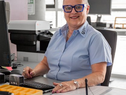 In der Patientenaufnahme sitzt eine Mitarbeiterin am Schalter, das digitale Unterschriften-Pad vor sich.