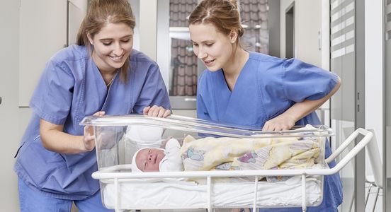 Zwei Pflegerinnen in der Geburtshilfe schauen auf ein Baby