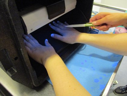 Auf dem Foto von einem Aktionstag der „Aktion Saubere Hände“ am Universitätsklinikum Ulm wird demonstriert, wie mithilfe der UV-Lampe sichtbar gemacht werden kann, ob die Hände korrekt desinfiziert wurden. (Quelle: Universitätsklinikum Ulm)