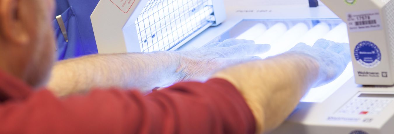 Ein Patient hält seine Hände in ein Gerät, das seine Haut mit Licht bestrahlt 