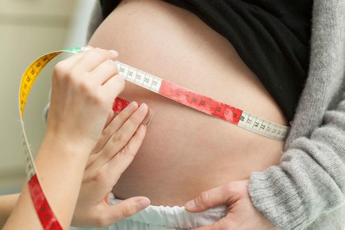 Der Bauch einer schwangeren Frau wird mit einem Maßband vermessen
