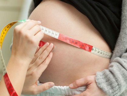 Der Bauch einer schwangeren Frau wird mit einem Maßband vermessen