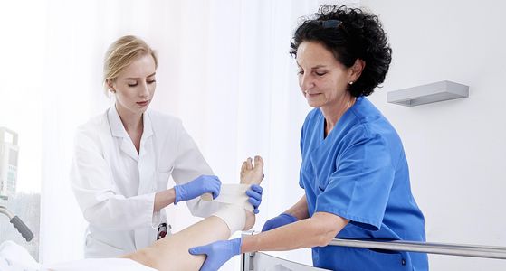 Eine Ärztin verbindet zusammen mit einer Krankenpflegerin den Fuß eines Patienten