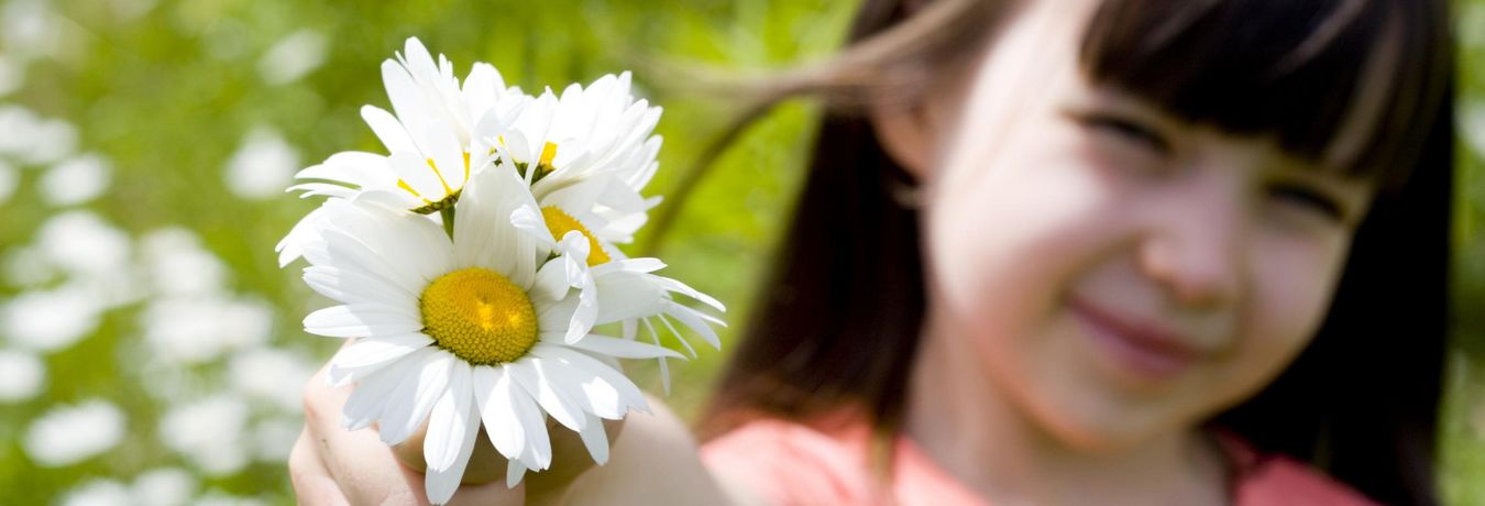 Junges Mädchen, das in die Kamera blickt und Blumen vor sich hält